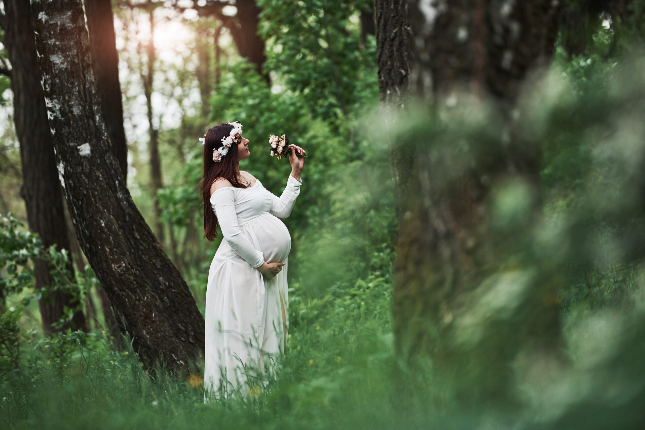 Sunlight and flowers. Beautiful pregnant woman in dress have a walk outdoors. Positive brunette.