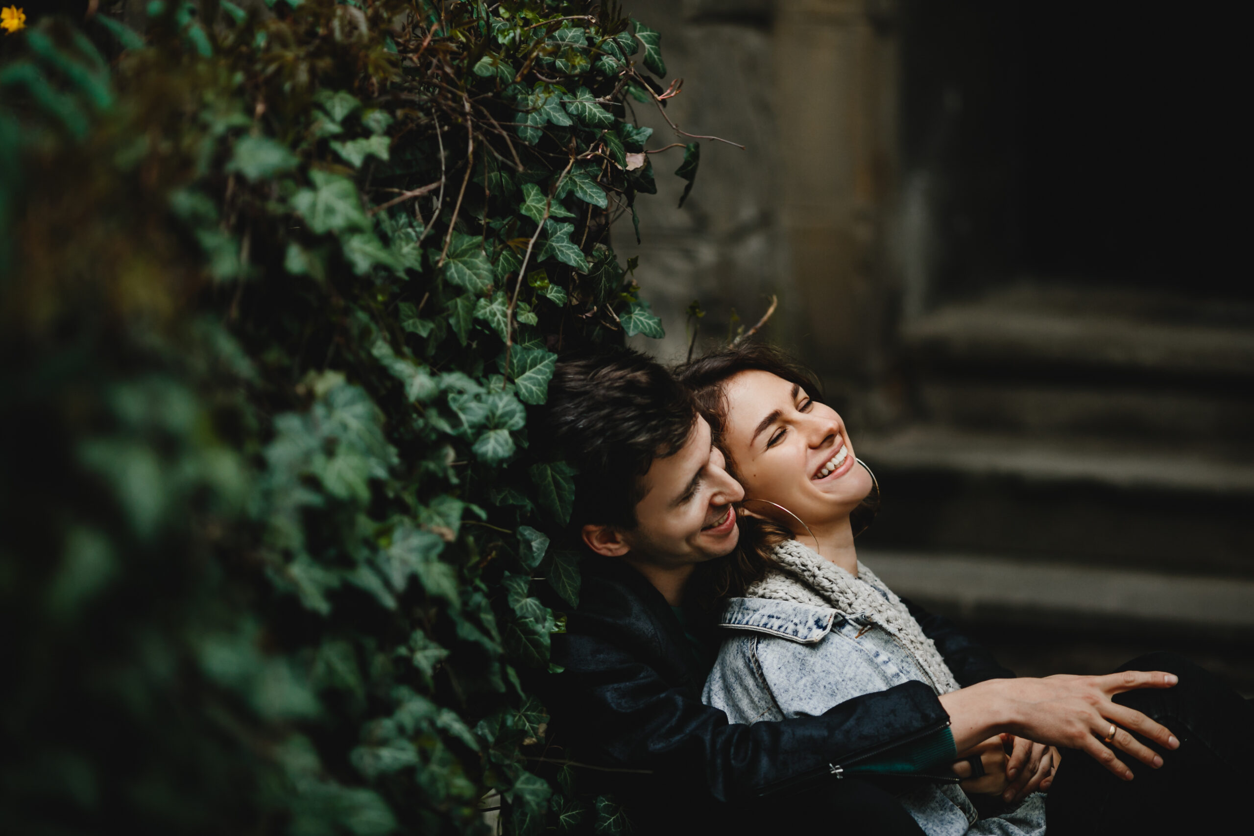 Young couple hugging sit near greenery wall and laughing